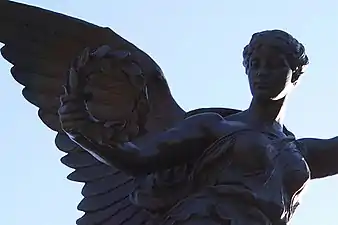 L'ange tient en sa main une couronne de laurier, symbole de la victoire.