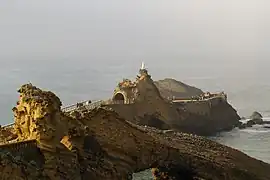 Vue d'un rocher sur la mer, surmonté d'une statue de la Vierge.