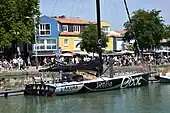 Vu de trois quarts arrière, en entier, voilier noir et argenté, amarré au quai.