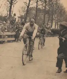 Cycliste franchissant la ligne d'arrivée marqué par l'effort et portant des lunettes opaques.