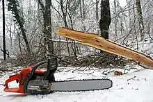 Une tronçonneuse posée sur la neige avec des arbres.