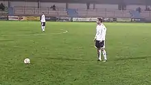 Photographie d'un joueur, portant un maillot blanc, s'apprêtant à tirer un coup franc.