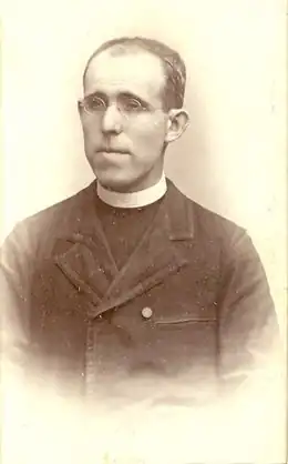 Photo noir et blanc d'un prêtre en clergyman, avec un visage en longueur, portant lunettes.