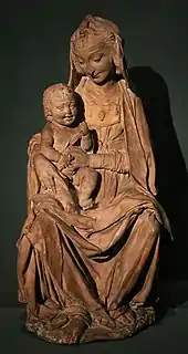 Sculpture représentant une femme tenant un bébé sur le genou droit et lui souriant.