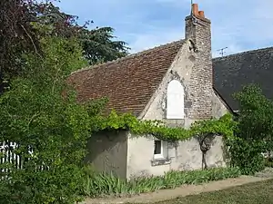 Photographie en couleurs et vue de trois-quarts d'une maison en pierres de taille de couleur beige et à toit aux pentes douces, la couverture d'un corps de logis visible en arrière-plan.