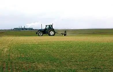 Paysage de plaine cultivé avec un tracteur au premier plan et une usine à l'arrière plan.