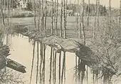 Extrait d'une ancienne carte postale en noir et blanc figurant une rivière et les paysages qui l'environnent.