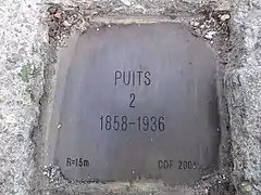 La plaque en laiton indiquant le nom du puits, et ses dates extrêmes.