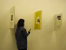 Une femme avec un smartphone devant 3 panneaux de verre perpendiculaires à un mur.