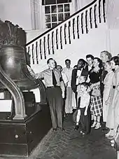Un homme en uniforme montre la Liberty Bell à plusieurs touristes habillés selon le style des années 1960.