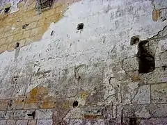 Photographe en couleurs d'un mur recouvert par places d'un enduit imitant des pierres et leurs joints.