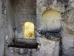 Photographie en couleurs d'une petite ouverture et d'un évier en pierre dans un mur.