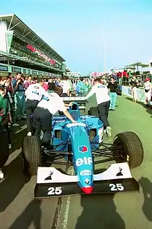 Photo vue de devant de la Ligier JS39B, bleue à l'aileron avant blanc et noir, poussée par des mécaniciens