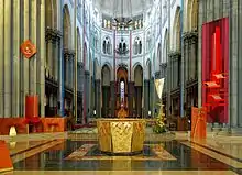 Photographie en couleurs du chœur vu de face avec au premier plan l'autel octogonal, à gauche la cathèdre et à droite l'ambon.