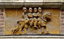 Plaque gravée dans la pierre, et en partie endommagée, placée au-dessus d'une devanture et représentant quatre hommes sur un même cheval