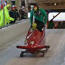 Vue d'un homme en combinaison verte entrant dans un bobsleigh rouge