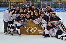 Photographie d'un groupe de joueurs de hockey sur glace à l'uniforme blanc, bleu marine et rouge célébrant leur victoire.