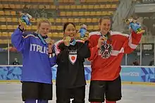 Photographie de trois joueuses de hockey sur glace présentant leur médaille olympique.