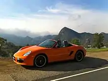 Photo de la Boxster "Limited Edition", orange avec des jantes noires, arrêtée sur le bord d'une route.