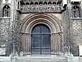 Un portail roman normand subsistant, délicatement sculpté, surmonté par une galerie des rois gothique.