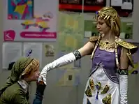 Femme en costume de princesse tendant le bras, alors qu'un homme accroupis lui fait un baiser sur la main.