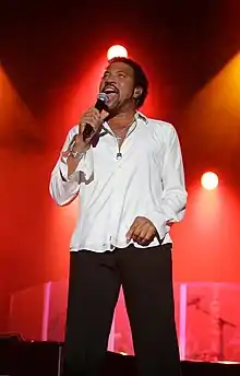 un chanteur sur scène en chemise blanche,pantalon noir tenant un microphone