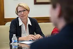 Photographie d'une femme blonde assise et portant des lunettes.