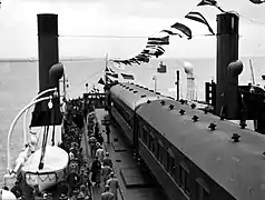photographie en noir et blanc d'un train transbordé par un ferry sur un fleuve.