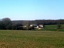 Photographie en couleurs de bâtiments isolés en bordure de vastes bois.