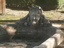 Photographie en couleurs d'un bassin dont l'arrivée d'eau est une tête humaine sculptée.