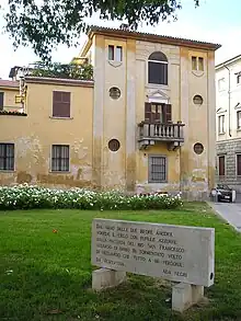 Pierre gravée en italien posée sur une pelouse, devant une maison dans une place.