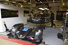 Photographie d'une voiture de sport-prototype, démontée, dans les stands, de trois-quarts.