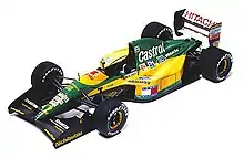 Vue plongeante sur une monoplace de Formule 1 en livrée bariolée jaune et verte, sur fond entièrement blanc.