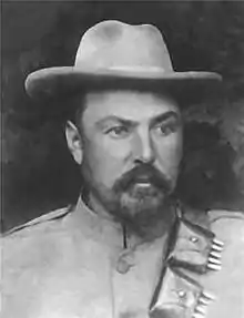 Louis Botha en tenue militaire, portant un chapeau de feutre à bords larges et une cartouchière remplie en bandoulière. Il porte une courte barbe sombre