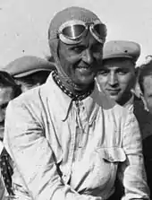 Photo de Louis Chiron souriant, en tenue de pilote, au milieu de la foule.