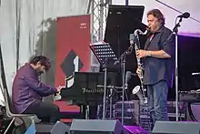 Sur une scène, Louis Sclavis joue de la clarinette basse, Benjamin Moussay est assis au piano