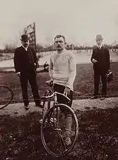 Photographie en noir et blanc d'un cycliste se tenant debout à côté de son vélo.