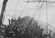 Photo en noir et blanc du pont d'un navire en pente, recouvert de soldats japonais faisant un salut militaire