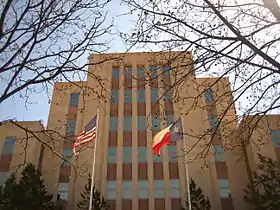 Vue d'un immeuble de couleur ocre avec des vitres en façade. Au premier plan, les drapeaux des États-Unis et du Texas.