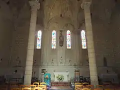 Photographie en couleur de chevet plat, montrant le maître-autel, quatre vitraux, des colonnes et une partie des voûtes.