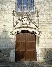 Vue de face d'un portail en pierre sculpté, encadrant une porte en bois.