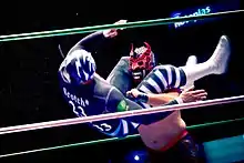 An action shot of La Sombra with his legs wrapped around Mephisto's head, flipping to throw him to the ground.