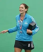 Une femme souriante, en survêtement, médaille autour du cou, tient une boîte contre elle.