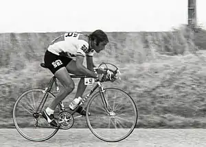Photographie en noir et blanc, d'un homme faisant du vélo, comportant une plaque de cadre avec le numéro 41