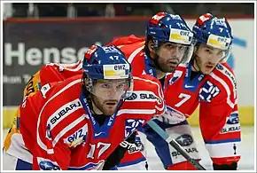 Photographie couleur représentant trois joueurs de hockey sur glace regardant vers la droite