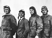 Photographie noir et blanc de quatre hommes debout en tenue de vol.