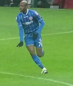 un joueur de football en tenue bleue en mouvement sur la pelouse d'un stade