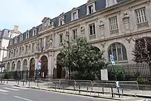 Photographie de la façade principale du lycée Janson-de-Sailly, à Paris, au cours des années 2000 et de la rue passante.