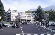 Photographie en couleurs d'un établissement scolaire et de groupes d'élèves à son entrée.