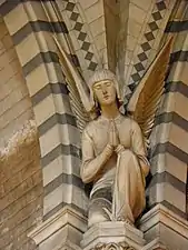 Photographie couleur de la statue d'un ange priant, posée sur la console qui soutient les arcs de la voûte.